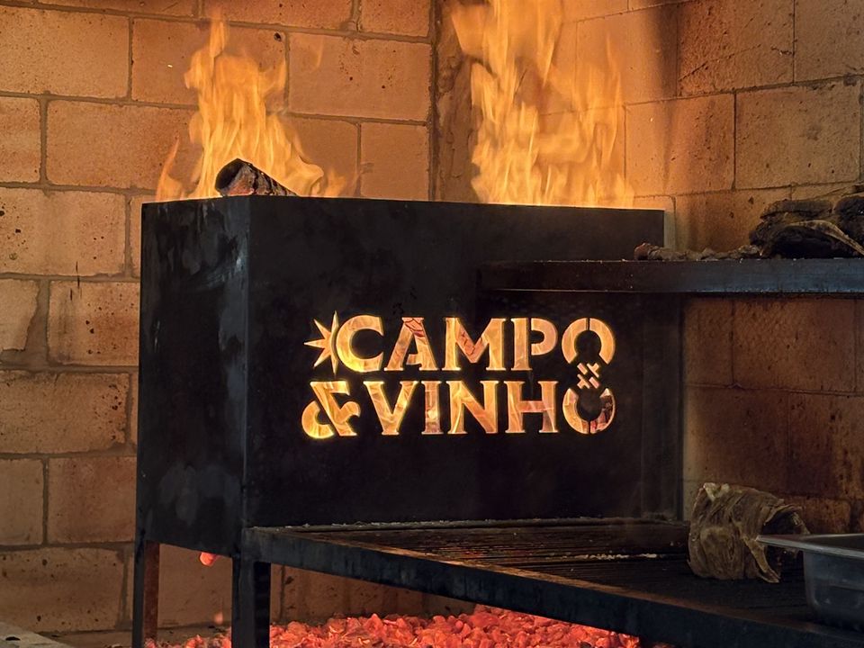 Churrasqueira acesa com o logo do Campo & Vinho recortado no ferro
